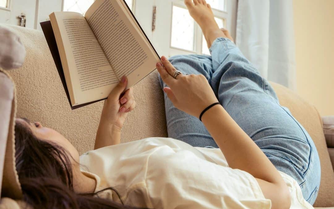 Reading woman relaxing on couch with book, comfortable home setting, wellness and self-care themes.
