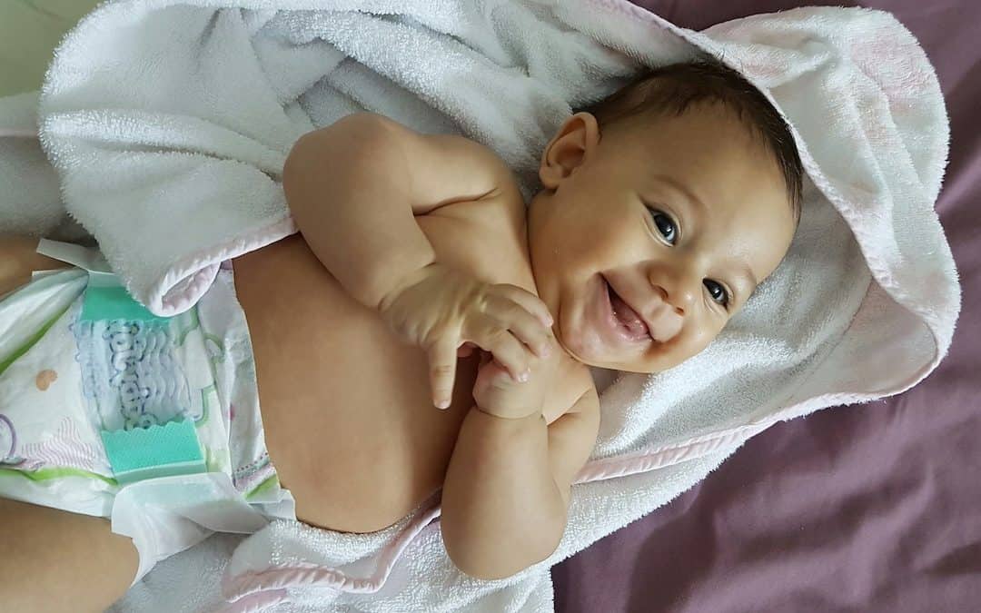 Smiling baby lying on towel after wellness treatment at Roots To Branches Whole Health Clinic.